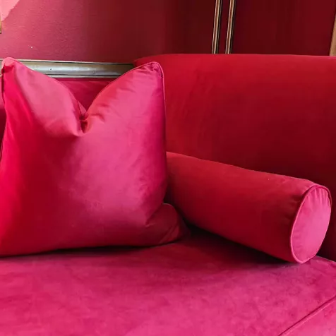 Hot pink velvet upholstery application on a vintage sofa, square decorative pillow, and round bolster pillow.